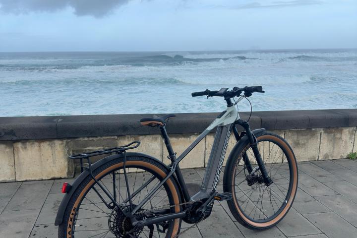 Bicycle parked on a paved seaside promenade with waves and cloudy sky in the background.
