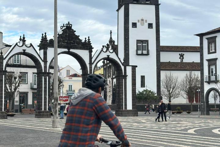 Person cycling near a clock tower and archway on a cloudy day.