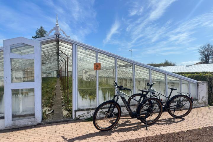 Two bicycles parked in front of a glass greenhouse under a blue sky.