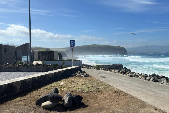 Coastal walkway beside ocean waves and rocky shoreline under a clear blue sky.