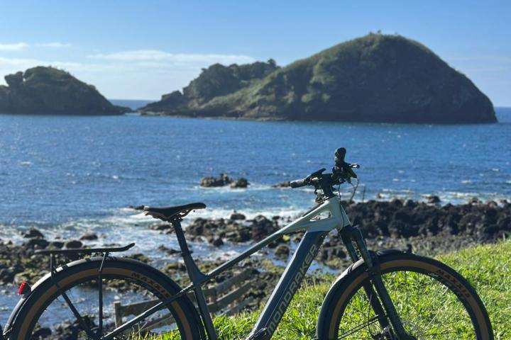 Mountain bike on grassy hill overlooking ocean and islands on a sunny day.
