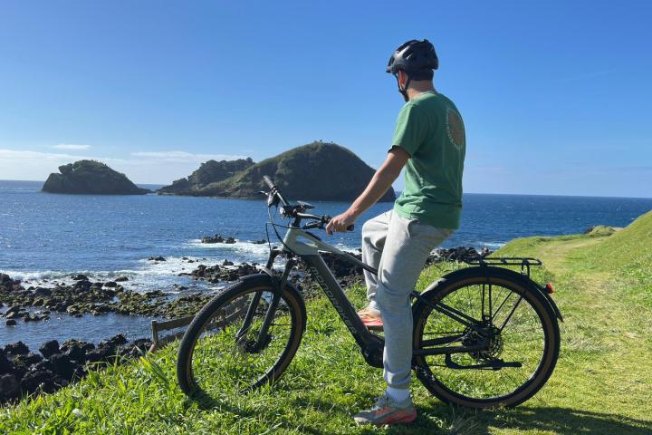 Person on a bike overlooking a coastal landscape with grassy hills and a blue ocean.