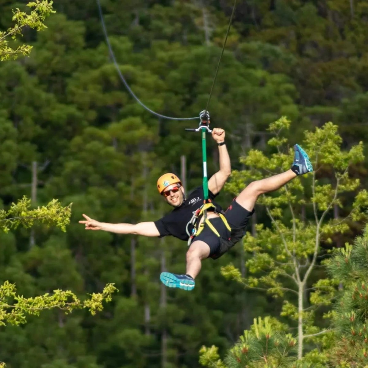 Person ziplining through forest, smiling and stretching arm outward.