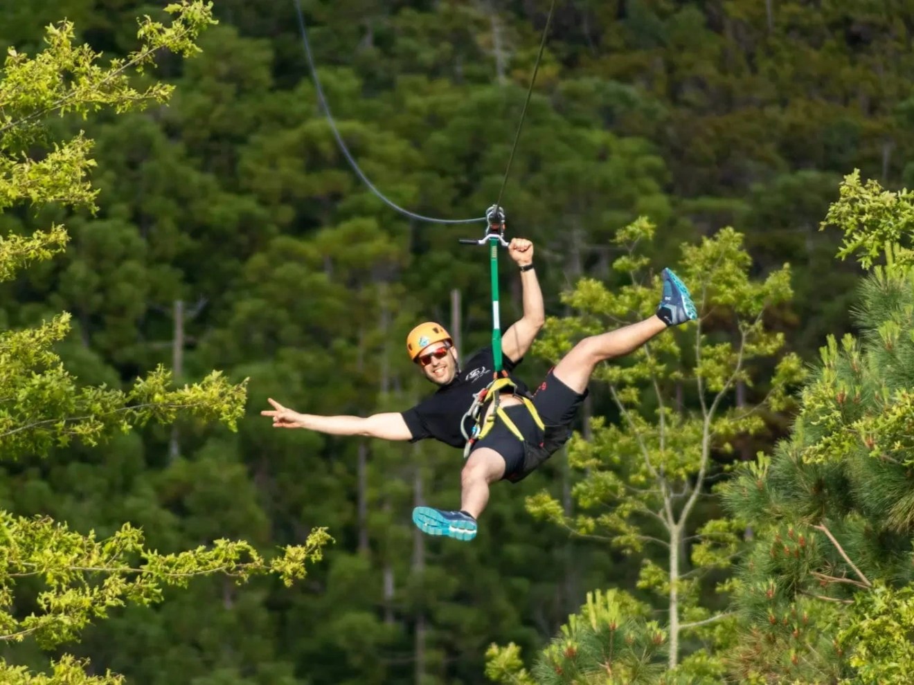 Person ziplining through forest, smiling and stretching arm outward.